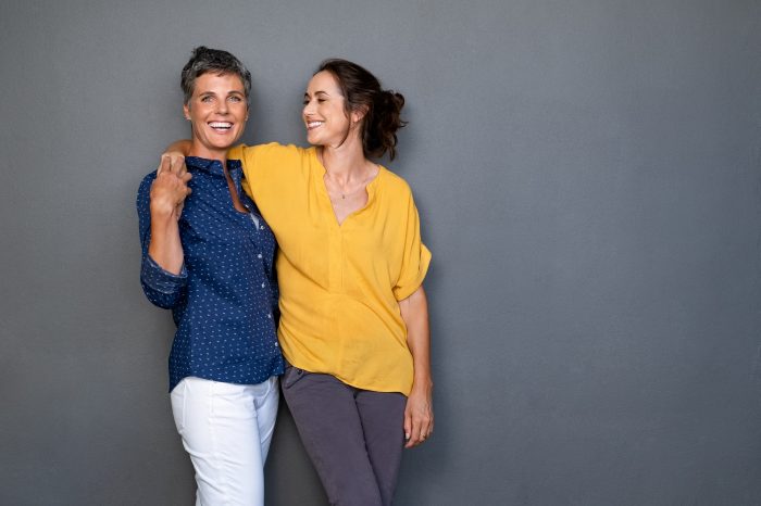 Mature happy women embracing each other against a grey wall.
