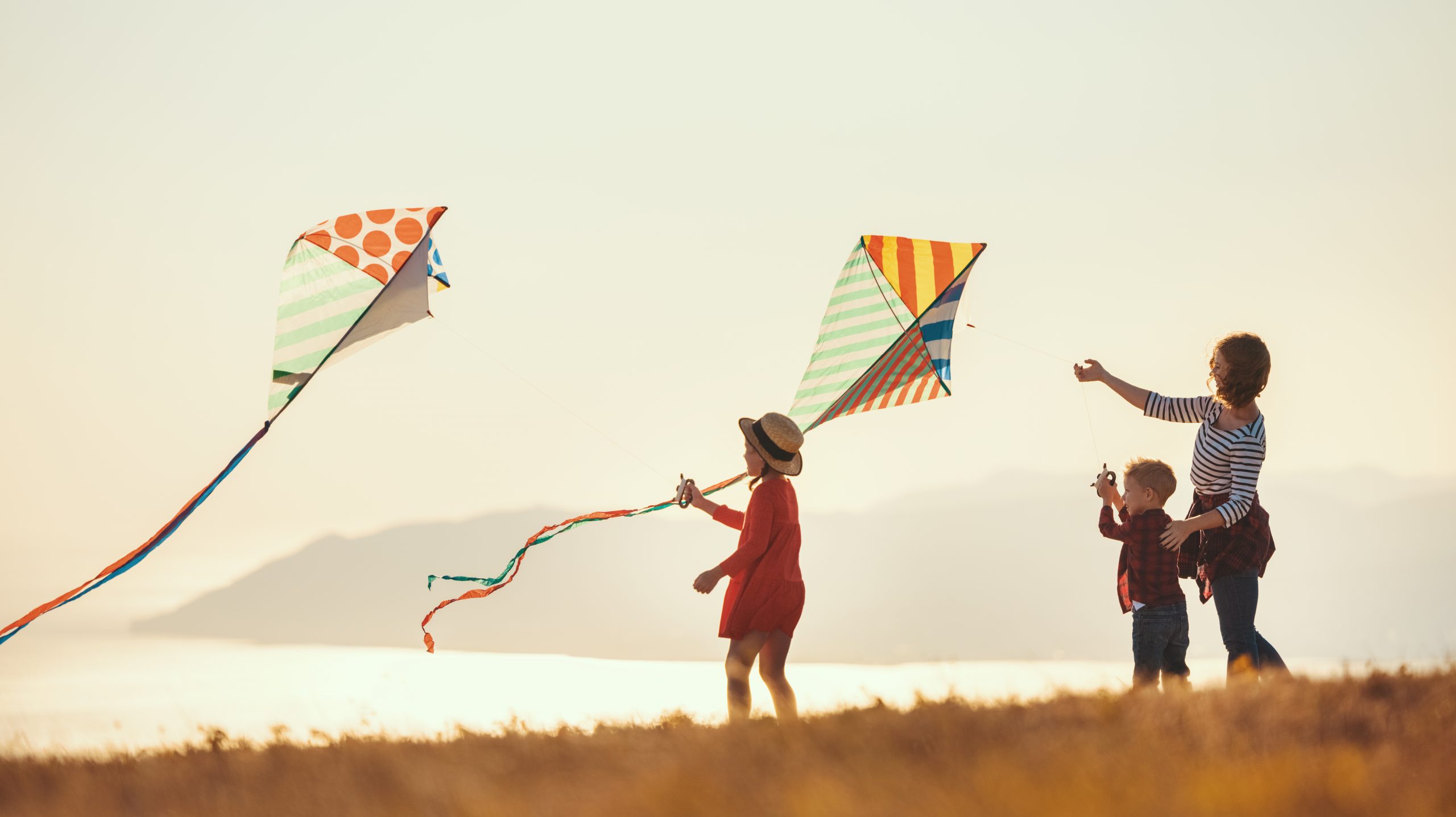 A young mother, daughter and son flying a kite by the ocean.