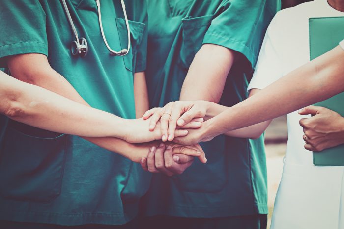 A group of doctors and nurses holding hands in the centre of the group.
