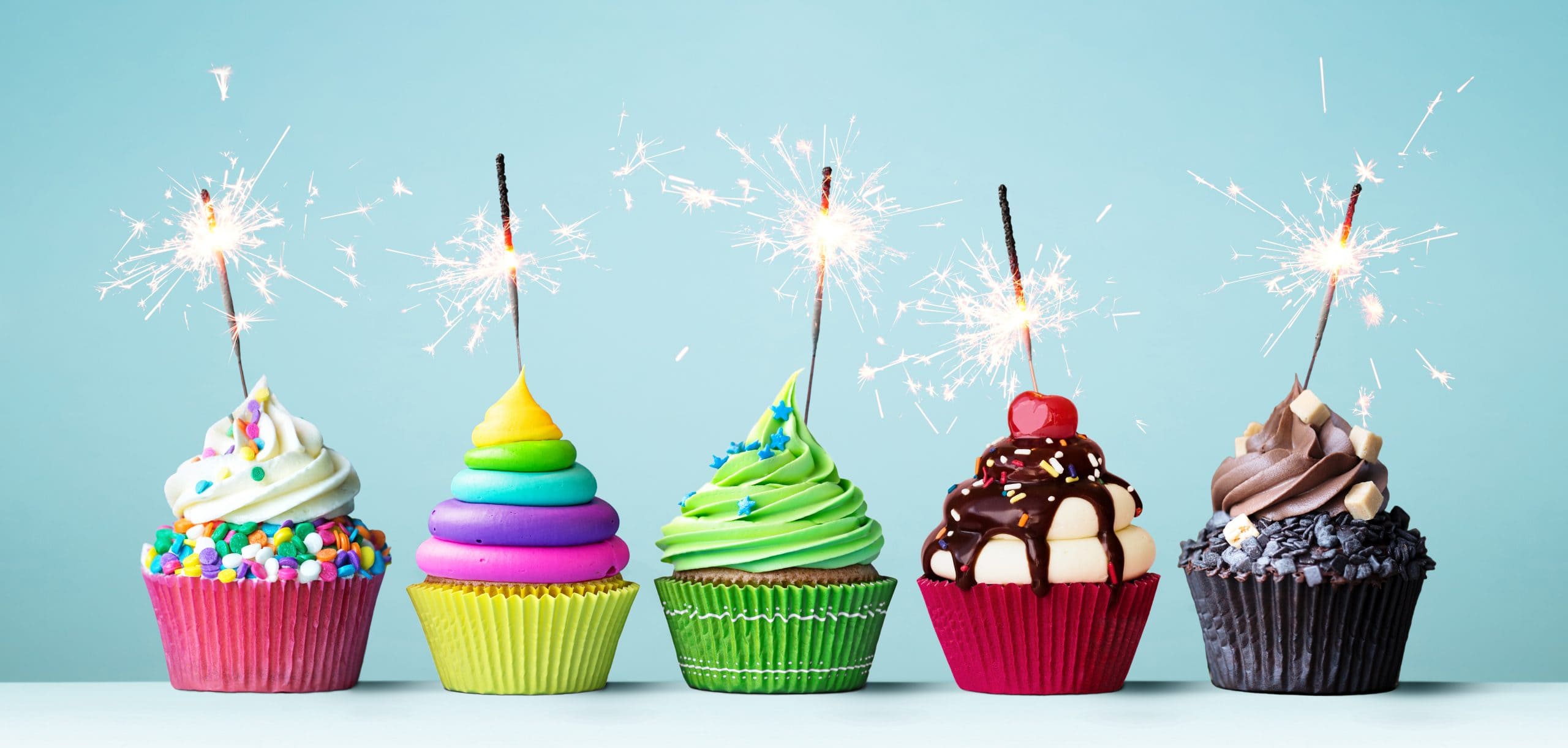 A row of different types of cupcakes all with sparklers lit.