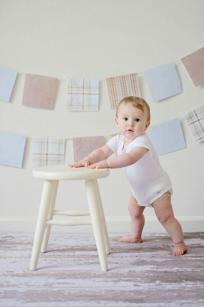 A small baby taking their first steps, holding onto a stool.